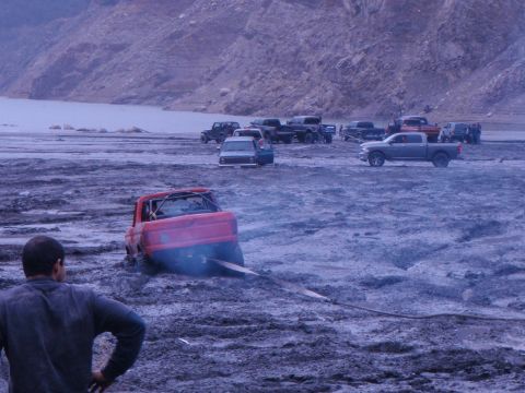 1978 Ford Bronco - Several vehicles are gathered in a muddy, barren landscape, with one red truck stuck and being towed.