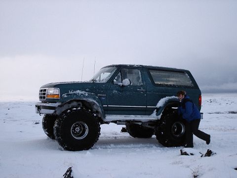 1996 Ford Bronco - A person leans on the oversized rear tire of a lifted Ford Bronco in a snow-covered landscape.