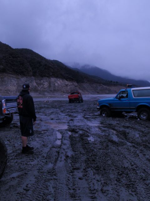 1978 Ford Bronco - Several off-road vehicles are parked in a muddy, desolate landscape under a cloudy sky.