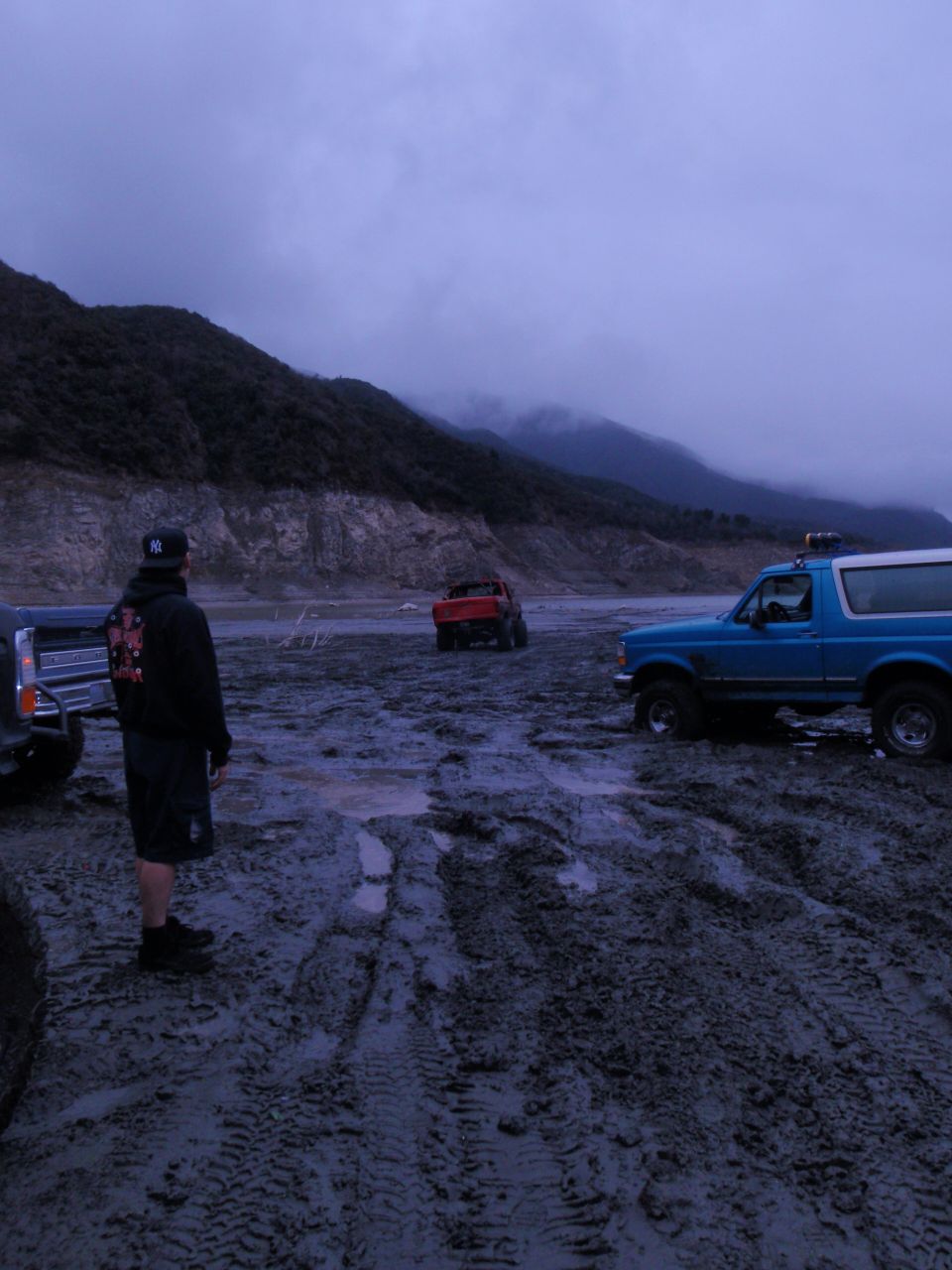 Blue SUV parked in muddy terrain with mountains in background