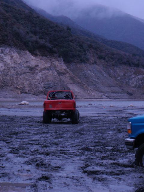 1978 Ford Bronco - Two trucks are parked in a muddy, desolate area with hills in the background.
