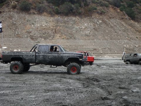 1978 Ford Bronco - Multiple off-road vehicles navigate a muddy terrain under a rocky hillside.