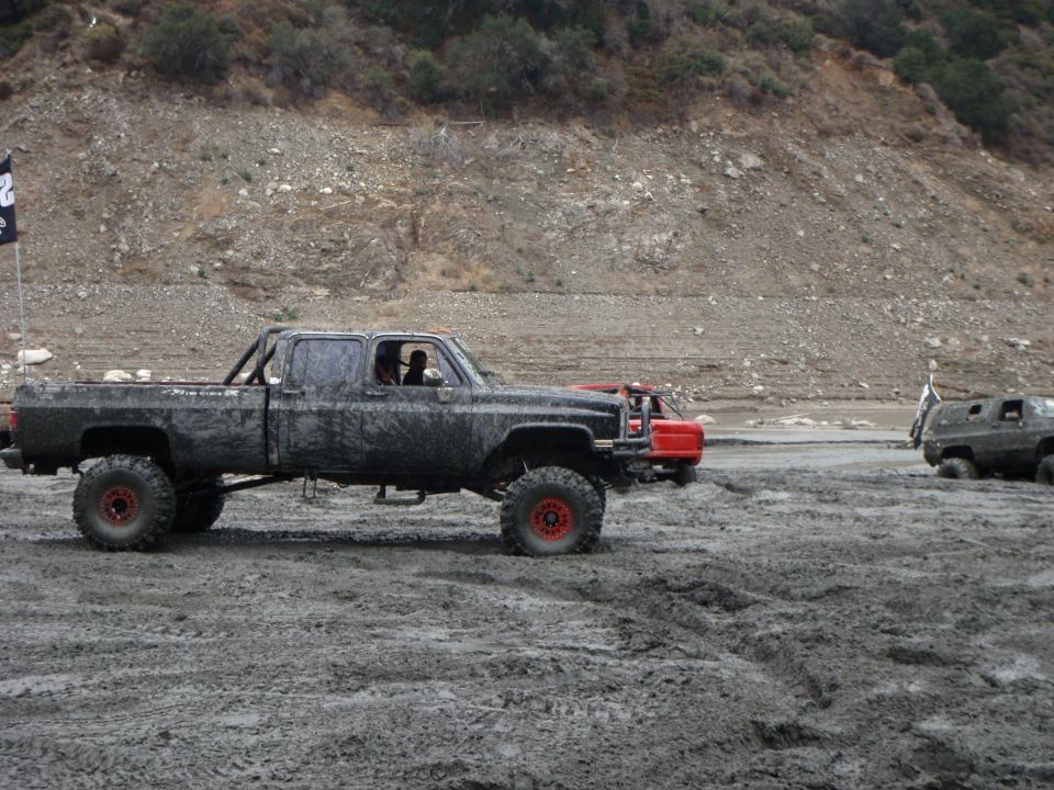 Mud-covered pickup truck with large tires and roll bar, side view