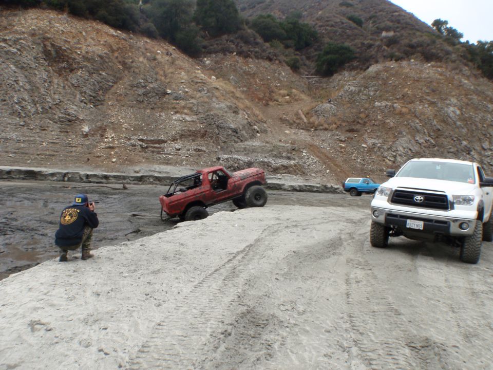 Red off-road truck stuck in mud with a person photographing it