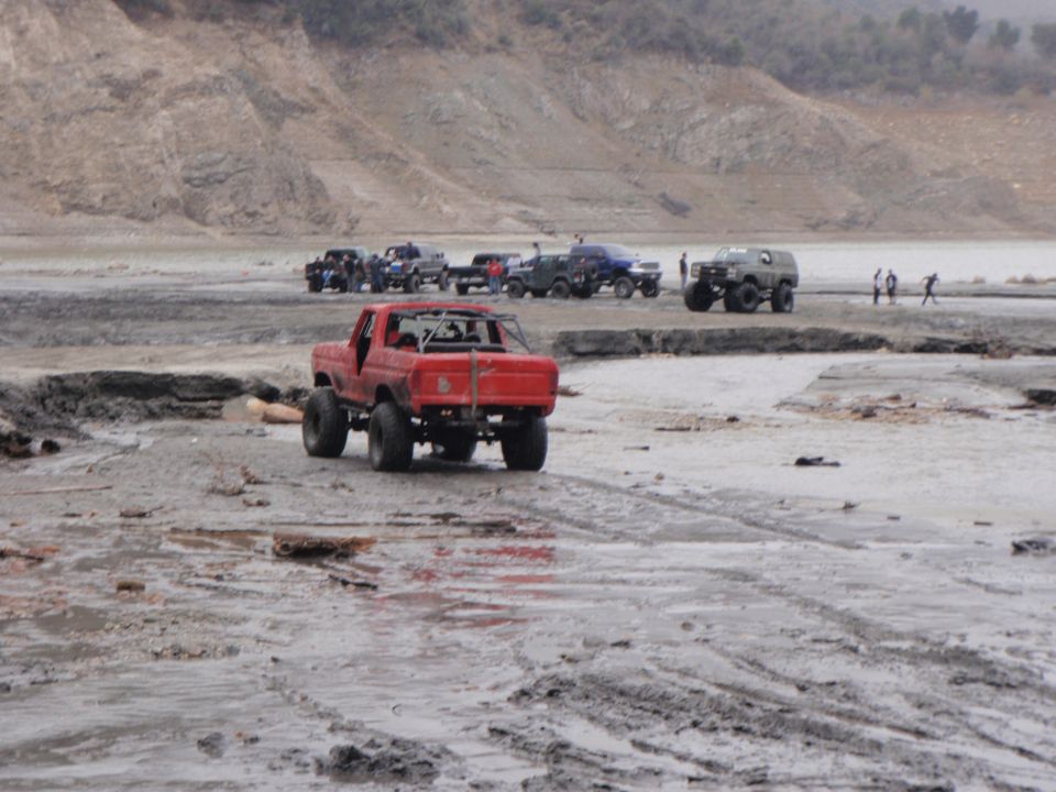 Red 1978 Ford Bronco modified for off-roading, rear view. Several other off-road vehicles in background
