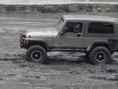 1978 Ford Bronco - A man drives a Jeep Wrangler Rubicon through a muddy terrain.