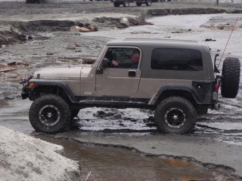 1978 Ford Bronco - A Jeep Wrangler Rubicon navigates a muddy terrain with a spare tire mounted on the rear.