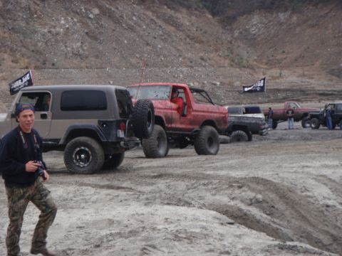 1978 Ford Bronco - A red 1978 Ford Bronco is seen off-roading with other vehicles in a muddy, hilly terrain.