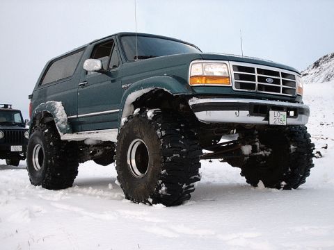 1996 Ford Bronco - A heavily modified green Ford Bronco with massive tires navigates a snowy landscape.