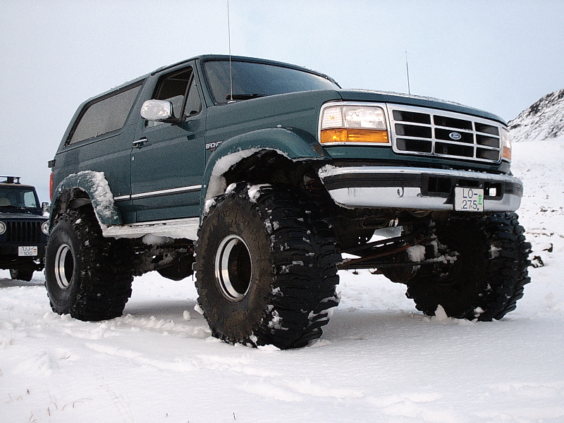 Lifted green Ford Bronco on large off-road tires in snow, front 3/4 view