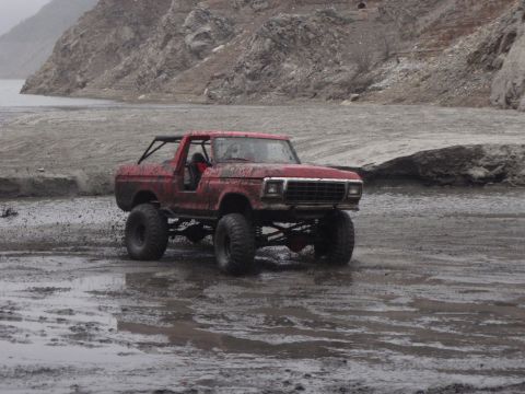 1978 Ford Bronco - A red 1978 Ford Bronco navigates a muddy terrain with a rocky hillside in the background.