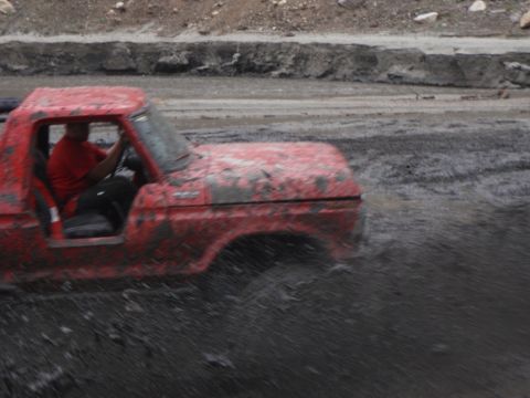 1978 Ford Bronco - A red pickup truck navigates a muddy terrain, kicking up water and dirt.