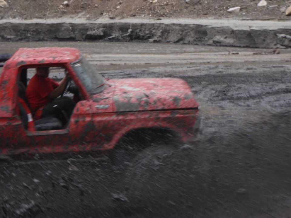 Red pickup truck with mud splattered on its body driving through a muddy track