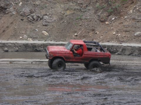 1978 Ford Bronco - A red 1978 Ford Bronco navigates a muddy off-road course, kicking up spray as it goes.