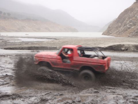 1978 Ford Bronco - A red 1978 Ford Bronco kicks up mud as it drives through a muddy terrain.