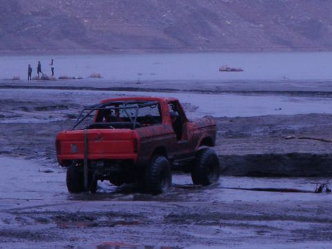 1978 Ford Bronco - A red 1978 Ford Bronco is stuck in the mud near a body of water with people in the background.