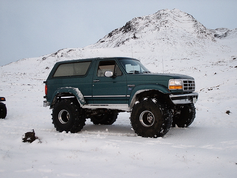 Green lifted two-door Ford Bronco on big tires in snowy mountain setting