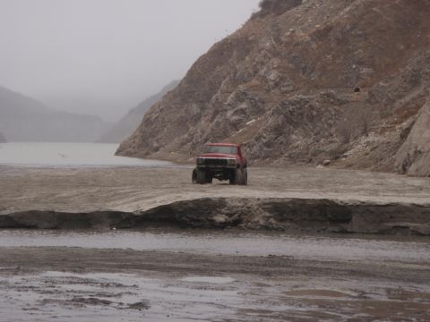1978 Ford Bronco - A red pickup truck is parked on a dirt road with a lake and mountains in the background.