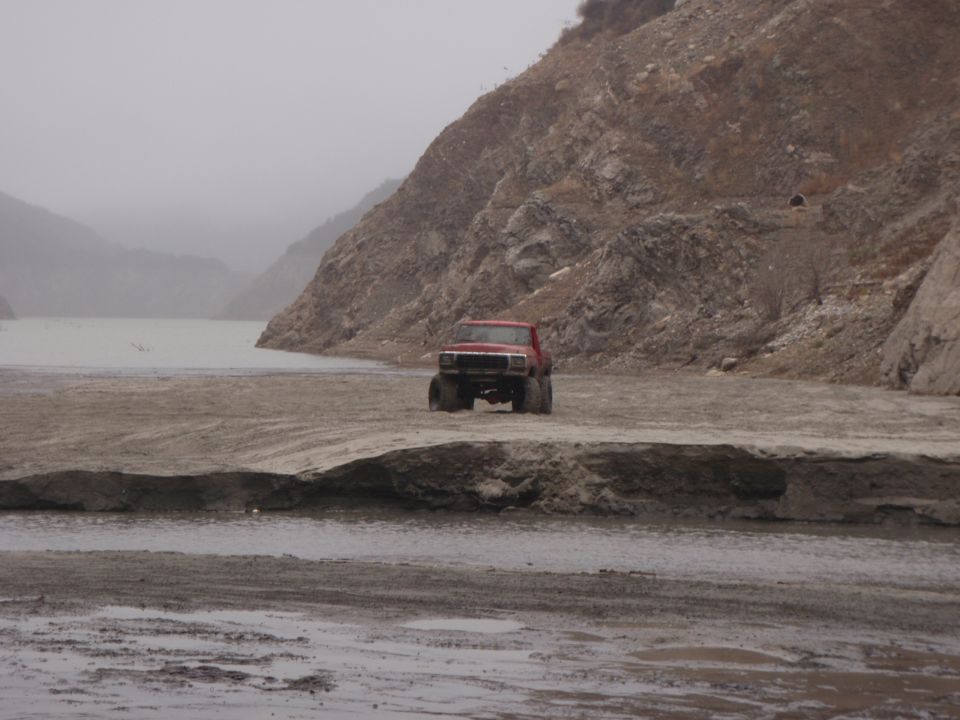 red pickup truck on dirt road near body of water and rocky hills