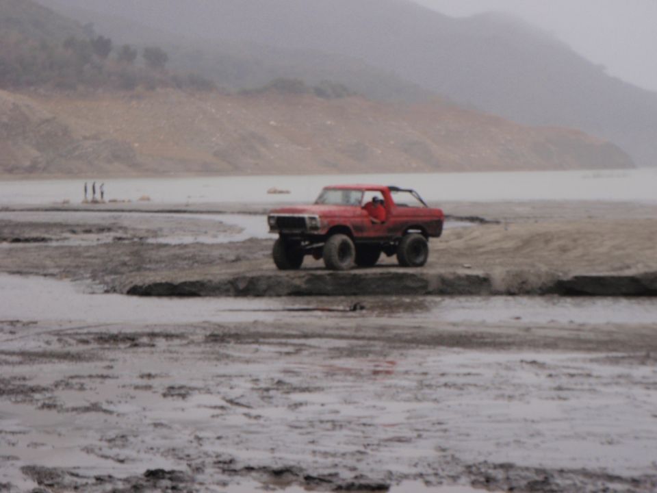 Red 1978 Ford Bronco with lifted suspension and off-road tires parked on a muddy embankment
