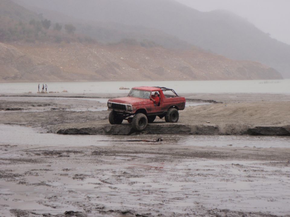 Red 1978 Ford Bronco off-roading on a muddy shore