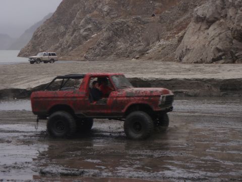 1978 Ford Bronco - A red 1978 Ford Bronco navigates a muddy terrain with another vehicle in the background.