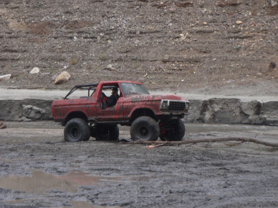 1978 Ford Bronco modified for off-roading, with large tires and a roll cage, driving through mud