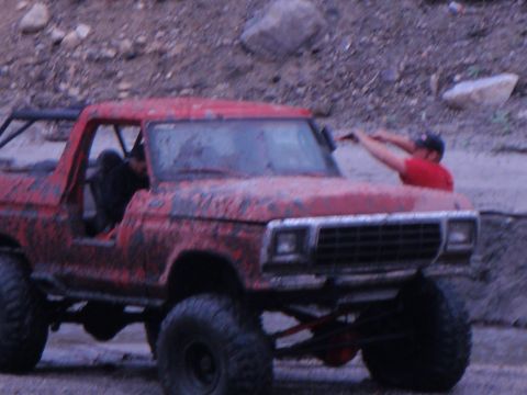 1978 Ford Bronco - A mud-covered 1978 Ford Bronco is shown from a three-quarter front angle with a person reaching towards the windshield.