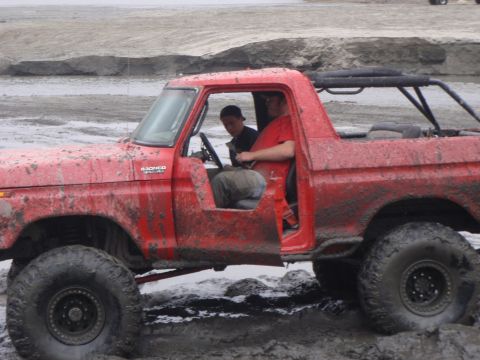 1978 Ford Bronco - A red 1978 Ford Bronco is stuck in the mud with two people inside.