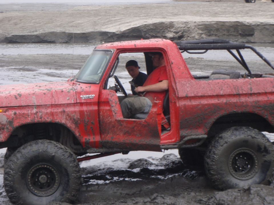 red 1978 Ford Bronco with two guys inside, stuck in mud