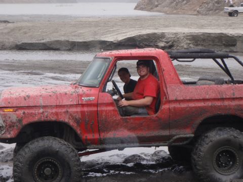1978 Ford Bronco - A mud-covered 1978 Ford Bronco navigates a wet, muddy terrain with two people inside.