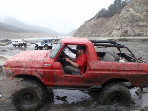 1978 Ford Bronco - A red 1978 Ford Bronco navigates a muddy terrain, with other off-road vehicles visible in the distance.