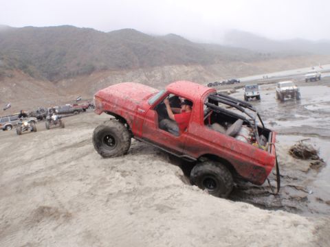 1978 Ford Bronco - A red 1978 Ford Bronco navigates a muddy, off-road terrain with other vehicles in the background.