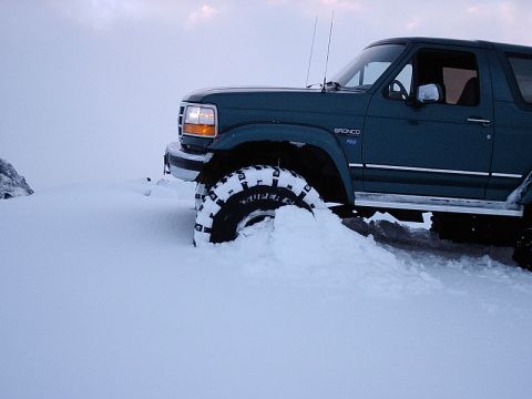 1996 Ford Bronco - A 1996 Ford Bronco is partially submerged in snow, with its front tire deeply embedded.