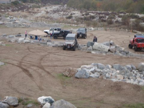 1978 Ford Bronco - Multiple off-road vehicles are gathered in a dirt lot with rocky terrain and a shaded tent area.