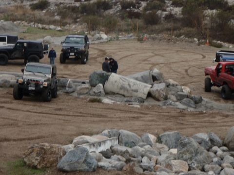 1978 Ford Bronco - Multiple off-road vehicles are gathered on a dirt lot, with large rocks and hills visible in the background.
