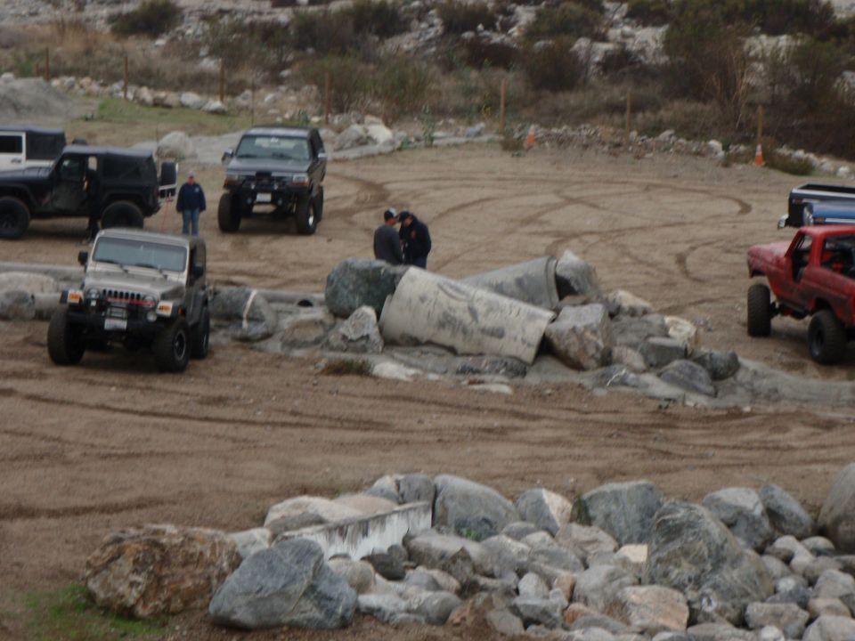 Several off-road vehicles parked on a dirt lot with rocks and hills in the background