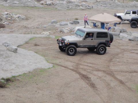 1978 Ford Bronco - A silver Jeep Wrangler TJ is parked on a dirt lot with other vehicles and a tent visible.