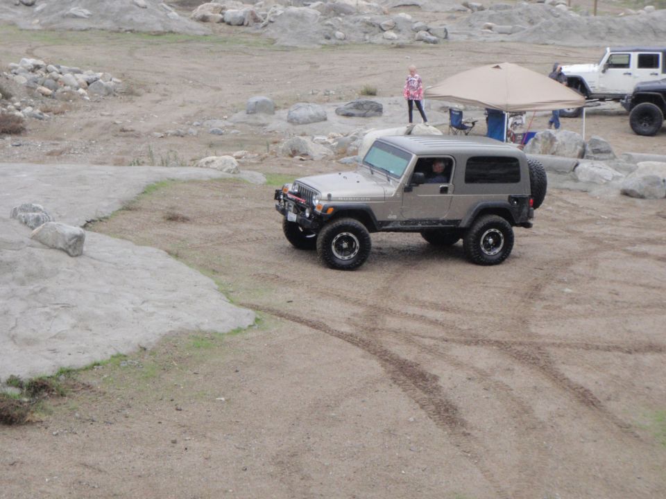 Silver Jeep Wrangler TJ parked on dirt with tire tracks. Another Jeep and a tent are in the background