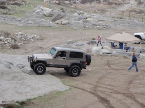 1978 Ford Bronco - A Jeep Wrangler navigates a rough, off-road terrain with people nearby.