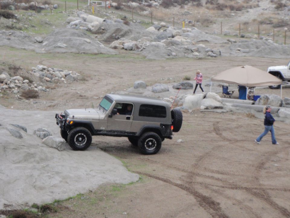Gray Jeep Wrangler with a spare tire on the back, driving on a rocky trail