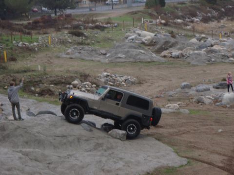 1978 Ford Bronco - A Jeep Wrangler tackles a challenging off-road course with a person watching.