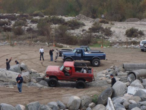 1978 Ford Bronco - Two trucks are seen off-roading in a rocky, outdoor area with several people observing.
