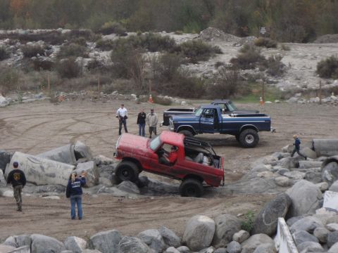 1978 Ford Bronco - A red 1978 Ford Bronco navigates a rocky obstacle course with a blue pickup truck in the background.