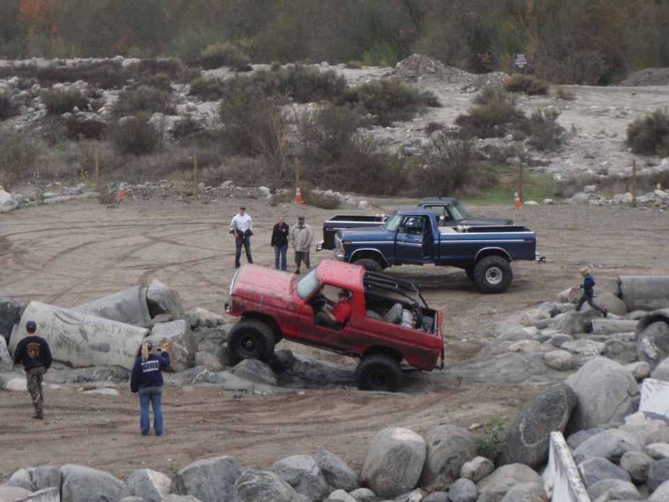 Red 1978 Ford Bronco off-roading over rocks, driver visible