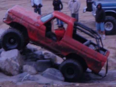 1978 Ford Bronco - A red off-road vehicle navigates a rocky terrain, while another vehicle waits in the background.