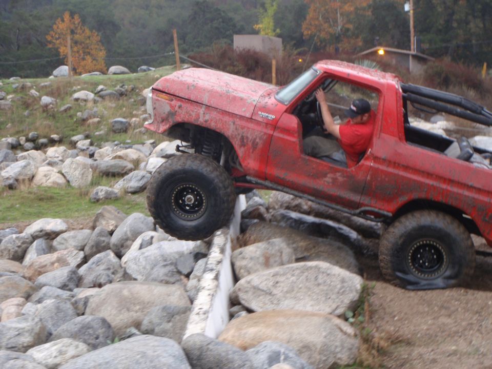 1978 Ford Bronco climbing over a rock obstacle course, driver visible