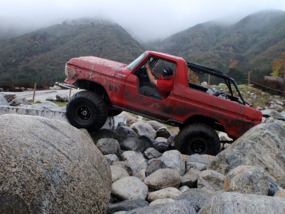 Red 1978 Ford Bronco off-roading over large rocks