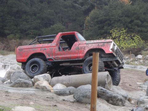1978 Ford Bronco - This modified SUV is navigating a challenging rocky terrain with large concrete pipes as obstacles.
