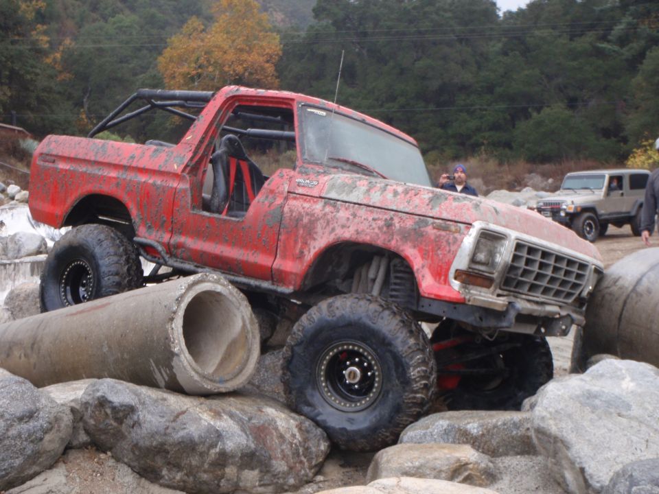 Red 1978 Ford Bronco on rocks with concrete pipes, another SUV in background